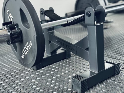 Ein Kunde zeigt die schwarze Deadlift Station, die eine Langhantel mit einer 10-kg-Scheibe auf einem Fitnessboden hält.