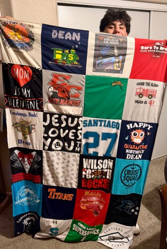 A person holding up a large, colorful Project Repat T-Shirt Quilt made from a collage of t-shirts and jerseys.