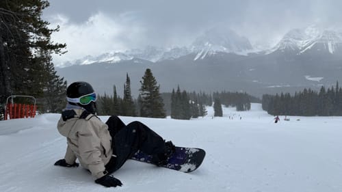 Reviewer sitting on a snowy slope wearing the black baggy waterproof snow pants with a snowboard.