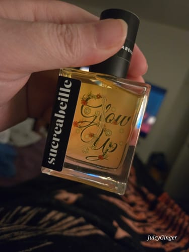 Reviewer holding a square bottle of Glow Up perfume with golden liquid.