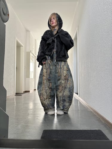 Reviewer showing the baggy fit of the Stain Embroidery Curved Jeans while standing in a hallway.