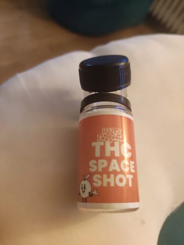 Kundenfoto des THC Space Shot Orange. Die kleine Flasche mit orangem Etikett steht auf einem Kissen.