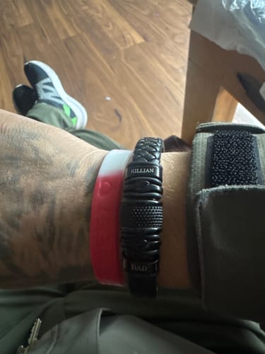 Customer wearing the personalized black bracelet on their wrist, engraved with 'KILLIAN' and 'DAD'.