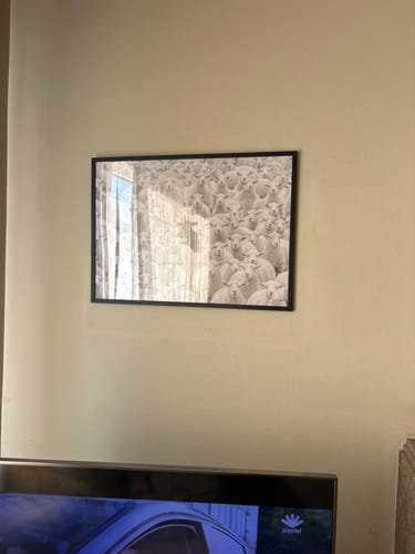 Customer's Black Oak Gallery Frame with a sheep print, hanging on a beige wall above a TV.
