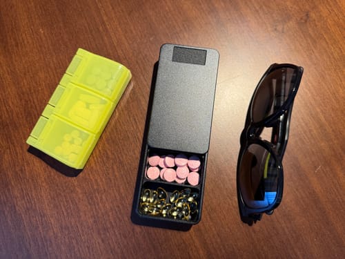Customer's open black metal pill case with vitamins, shown next to a yellow plastic case for comparison.