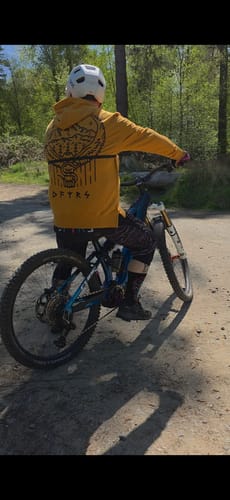 Reviewer on a bike trail wearing the yellow Heartbreaker Trailhood, showing the large graphic on the back.