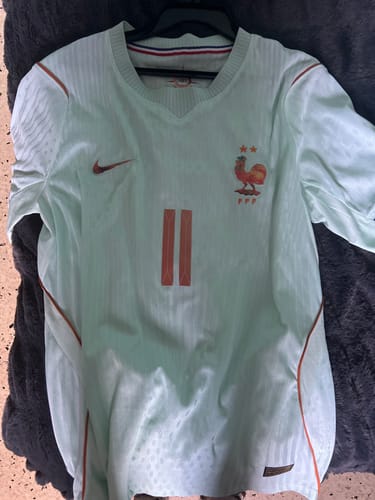 Client montrant le maillot 2026 France Extérieur player de couleur claire avec des détails orange, posé à plat.