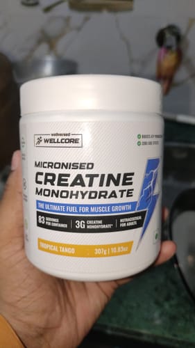 Customer holds a white tub of Wellcore Micronised Creatine Monohydrate, showing the Tropical Tango flavor.