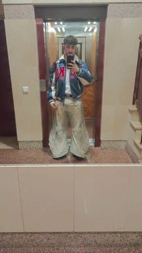 Reviewer taking a full-length mirror selfie wearing the light-colored, flared patchwork jeans.