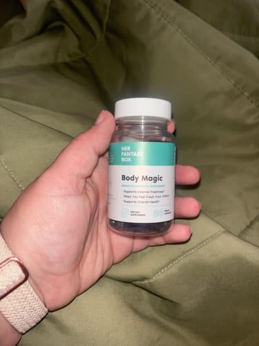 Customer holding a clear bottle of Body Magic Chlorophyll Pills against an olive green background.