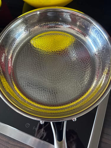 Ein Kunde zeigt die glänzende, gehämmerte Titanpfanne aus der Nähe auf einem Kochfeld.