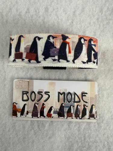 Customer's Boss Mode Bracelet and its collector's card, both showing illustrated penguins in coats carrying briefcases.