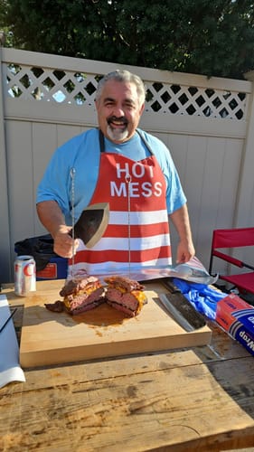 Reviewer in an apron smiling and holding the Daozi 8" Butcher Knife over a large, cut burger at an outdoor cookout.
