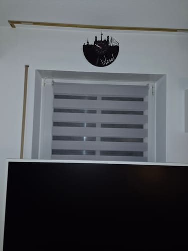 Rezensent zeigt die schöne, schwarze Vinyl-Wanduhr mit Wesel-Skyline an der Wand über einem Fenster.