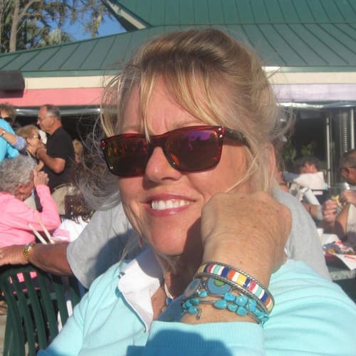 A happy reviewer with blonde hair and sunglasses smiling while sitting outdoors.