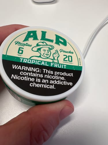 Customer holding the round, green and white tin of Tropical Fruit Nicotine Pouches.