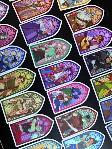 Customer's colorful custom vinyl stickers showing illustrated characters in a stained-glass design scattered on a dark surface.