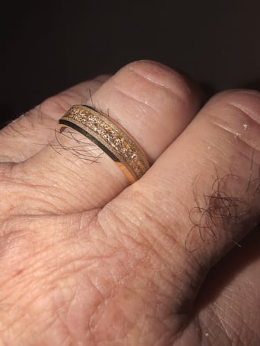 Close-up of a customer's hand wearing the Aureum ring, showing its textured gold foil inlay and dark edges.