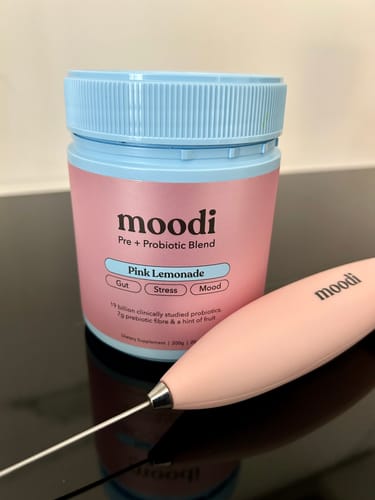 Customer's jar of Moodi Pink Lemonade Pre + Probiotic Blend with a pink branded frother on a black surface.