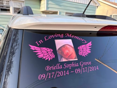 A customer's pink 'In Loving Memory' decal on a car window, featuring a photo inlay, wings, and custom text.