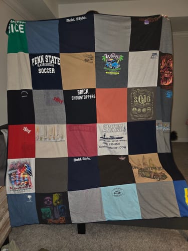 Customer holding up a large, multi-colored Premium T-Shirt Quilt made from various t-shirts indoors.