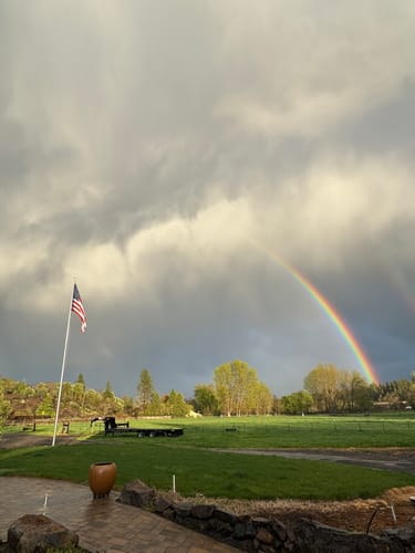 Customer's American flag on a flagpole in a field, with a bright rainbow arching under stormy clouds.