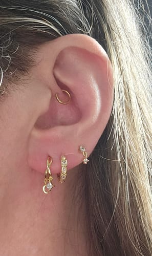 Customer's ear with multiple piercings, showing the gold Shapeshifter huggies in the second lobe piercing.