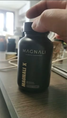 A customer holding the matte black bottle of Magnali X on a wooden desk.