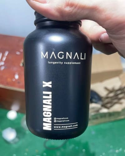 A customer's hand holding the matte black bottle of Magnali X longevity supplement.