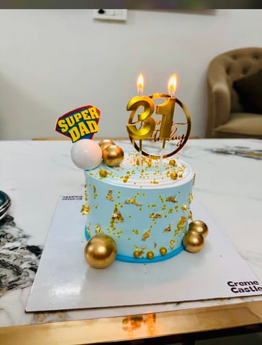 Reviewer's Golden Blue Cake with a 'Super Dad' topper and lit candles for a 31st birthday.