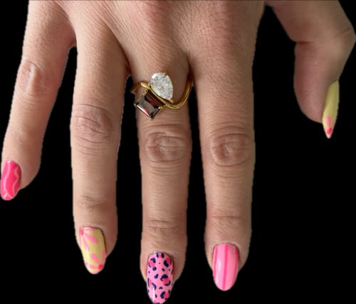 Customer's hand wearing the Navae Birthstone Ring. The gold ring has a clear pear-cut and a dark red radiant-cut stone.