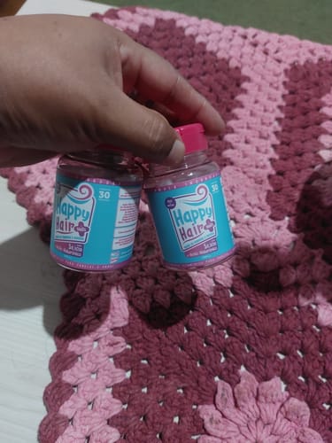 Cliente segurando dois potes do suplemento vitamínico Happy Hair sobre uma toalha de crochê.
