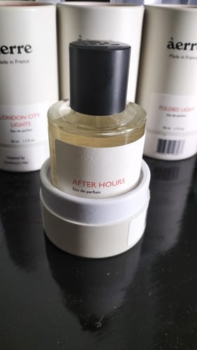 Customer's After Hours perfume bottle with a black cap, displayed on its white cylindrical box on a dark, reflective surface.