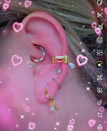 Customer wearing the gold Gaia Huggies with celestial charms in their first lobe piercing as part of an ear stack.