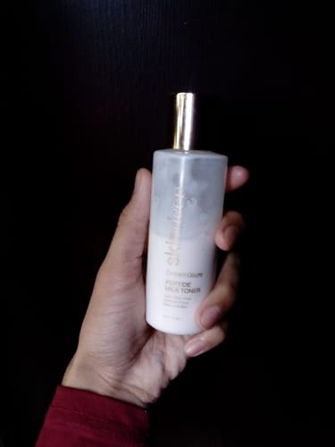 Customer holding the white bottle of DREAM GLAZE Peptide Milk Toner against a dark background.