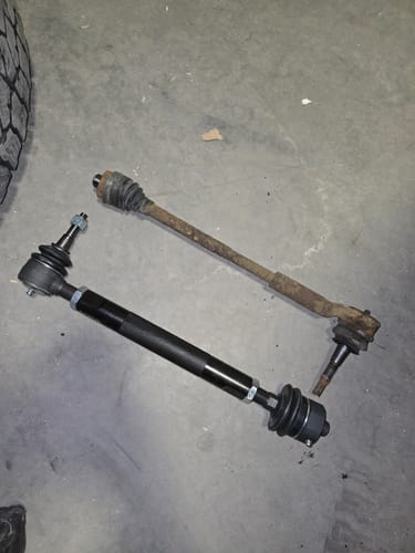 Customer compares the new black adjustable tie rod to the old, rusty original part on a concrete floor.