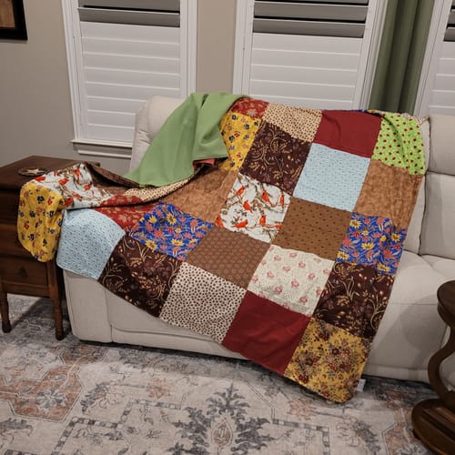 Customer's Project Repat T-Shirt Quilt made from colorful, patterned material scraps draped over a sofa.