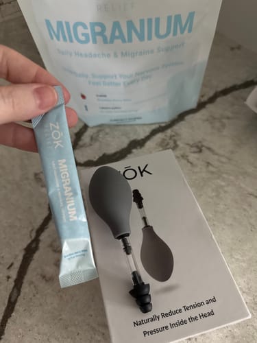 A reviewer's ZŌK Device and a packet of Migranium powder laid out on a kitchen counter.