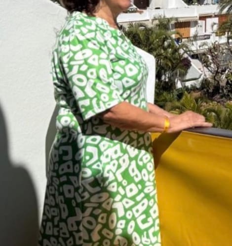 Recensent i den gröna lediga klänningen med vitt mönster, fotograferad från sidan utomhus.