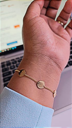 Customer's wrist wearing the gold Happiness Bracelet with delicate calligraphy charms.