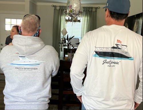 Reviewer and a friend show the back of their custom boat apparel, including a white Dri-Fit shirt and a grey hoodie.