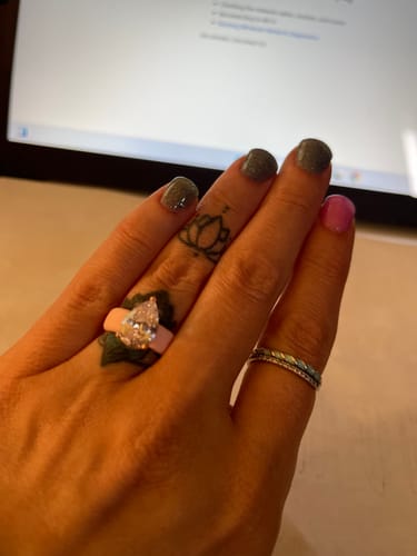 Reviewer's hand wearing the light pink Silicone Ring with its sparkly pear-cut stone at a desk.