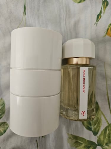 Recensore mostra il flacone di profumo ATRACTONE MUSK accanto alla sua confezione cilindrica bianca.