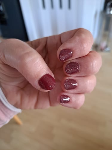 Die Hand eines Kunden mit einer dunkelroten Maniküre, veredelt mit dem UV Top Coat Silver Glitter Bold.