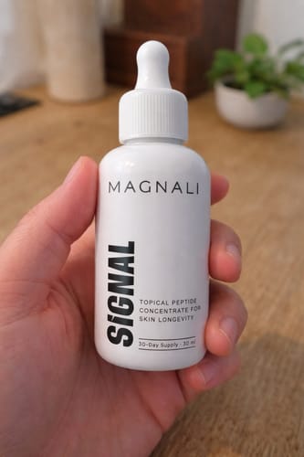 A reviewer holds the white dropper bottle of Magnali Signal topical peptide concentrate.