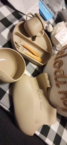 Partial view of a customer's personalized knitted basket, shown with other baby gift items on a checkered surface.