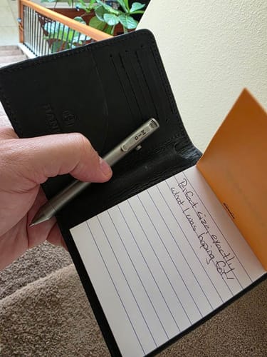 Reviewer holds the open black Notesman wallet in hand, showing the notepad with a handwritten message and a pen.