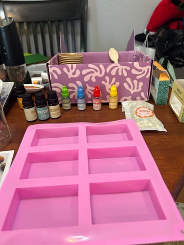 Reviewer's craft subscription box contents, with a pink soap mold and small colorful bottles on a table.