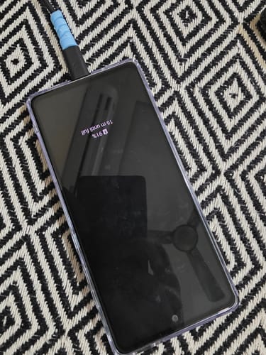 Customer's smartphone with the UltraShield Tempered Glass applied, charging on a black and white patterned surface.