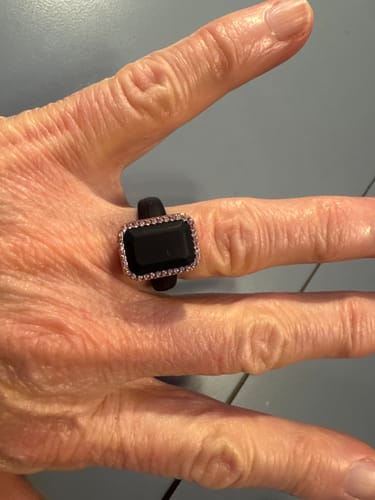A reviewer's hand wearing the black Emerald Silicone Ring with a rectangular stone and a halo of pink CZ stones.
